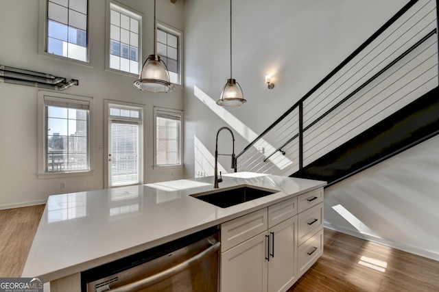 kitchen with pendant lighting, white cabinetry, sink, stainless steel dishwasher, and a center island with sink