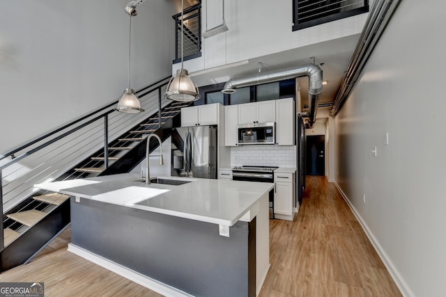 kitchen with appliances with stainless steel finishes, a towering ceiling, white cabinets, and decorative light fixtures