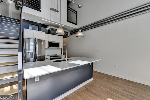 kitchen with sink, white cabinetry, hanging light fixtures, stainless steel appliances, and decorative backsplash