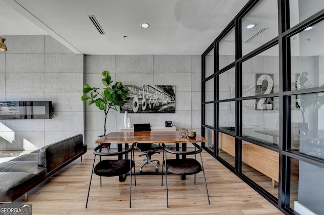 dining room with tile walls, light hardwood / wood-style flooring, floor to ceiling windows, and a healthy amount of sunlight