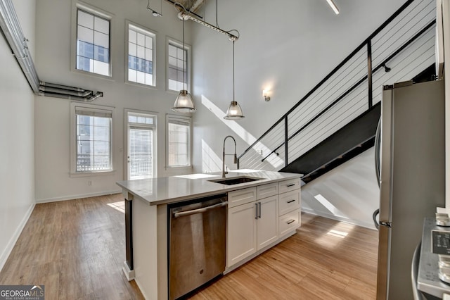 kitchen with a kitchen island with sink, hanging light fixtures, a towering ceiling, stainless steel appliances, and white cabinets