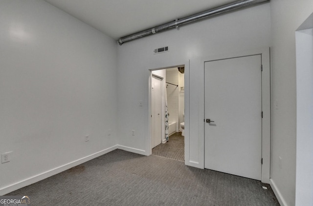 unfurnished bedroom featuring ensuite bathroom and dark colored carpet