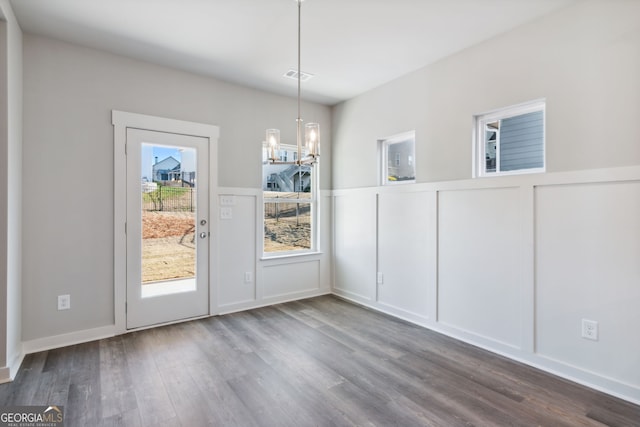 unfurnished dining area with an inviting chandelier, visible vents, a decorative wall, and wood finished floors