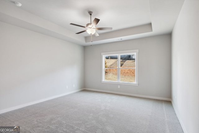 carpeted empty room with ceiling fan, a raised ceiling, visible vents, and baseboards