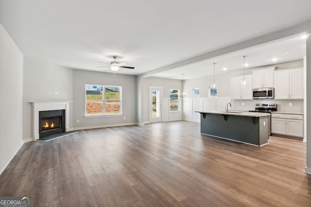 unfurnished living room featuring ceiling fan, wood finished floors, a sink, baseboards, and a lit fireplace