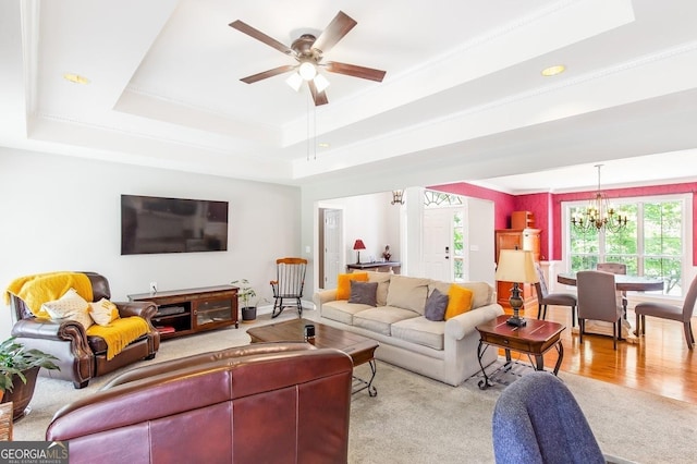 living room with a raised ceiling, ornamental molding, and ceiling fan with notable chandelier