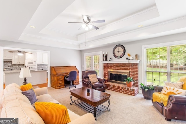 carpeted living room featuring crown molding, ceiling fan, a tray ceiling, and a fireplace