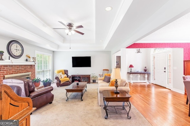 living room featuring a tray ceiling, a fireplace, ceiling fan, light hardwood / wood-style floors, and crown molding