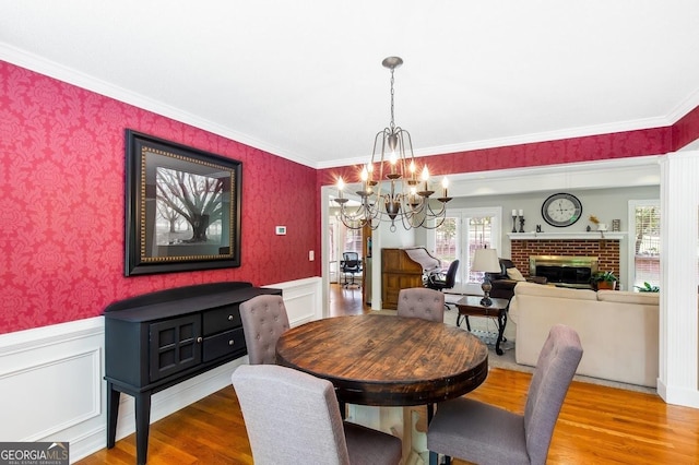 dining space with hardwood / wood-style floors, crown molding, a notable chandelier, and a brick fireplace