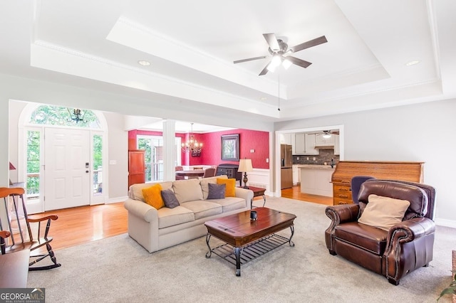 living room with a tray ceiling and ceiling fan with notable chandelier