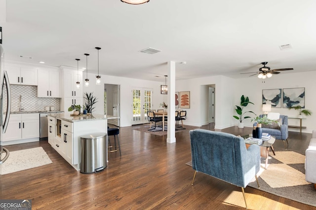 kitchen featuring a kitchen island, tasteful backsplash, white cabinets, hanging light fixtures, and light stone counters