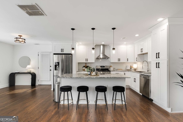 kitchen with pendant lighting, sink, white cabinets, stainless steel appliances, and wall chimney range hood