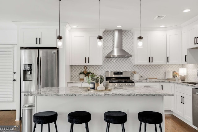 kitchen featuring pendant lighting, white cabinetry, appliances with stainless steel finishes, and wall chimney range hood