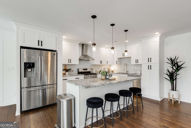 kitchen with white cabinetry, a center island, appliances with stainless steel finishes, pendant lighting, and wall chimney range hood