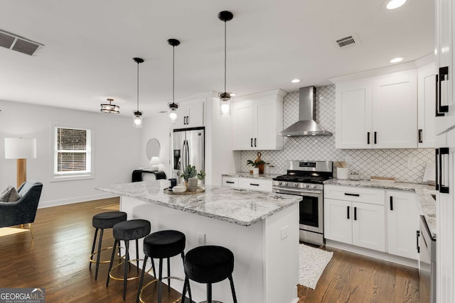 kitchen featuring appliances with stainless steel finishes, wall chimney range hood, white cabinets, and decorative light fixtures