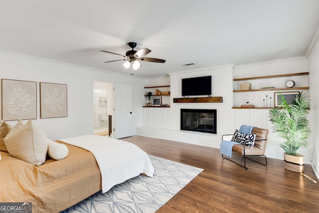 bedroom with ensuite bathroom, crown molding, a brick fireplace, ceiling fan, and hardwood / wood-style floors