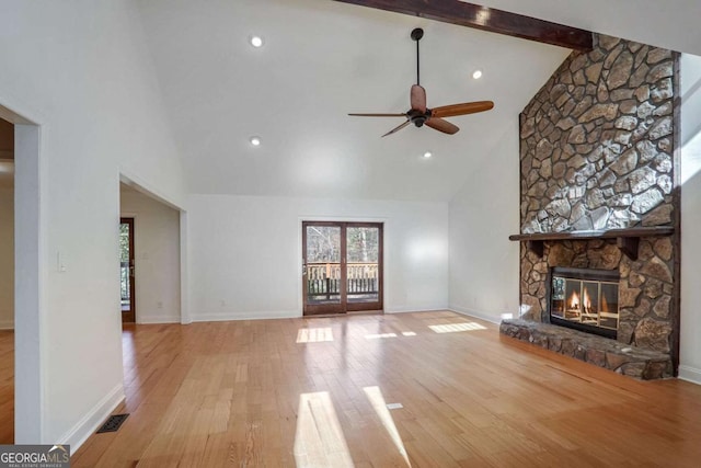 unfurnished living room with ceiling fan, high vaulted ceiling, light hardwood / wood-style floors, a stone fireplace, and beamed ceiling