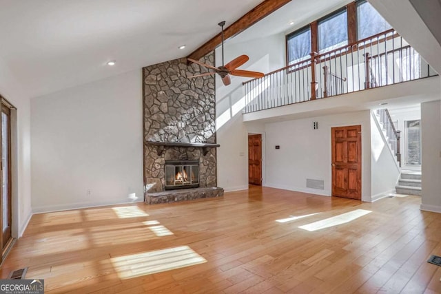 unfurnished living room featuring beamed ceiling, a stone fireplace, high vaulted ceiling, and light hardwood / wood-style floors