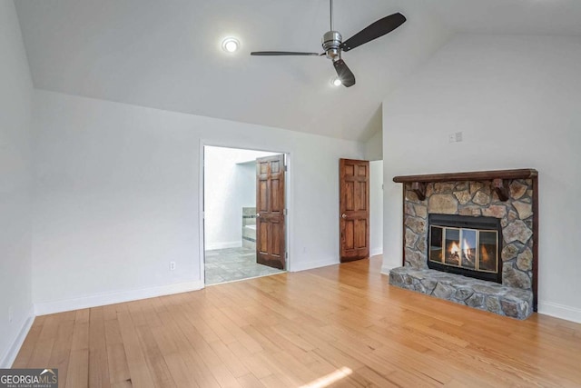 unfurnished living room with ceiling fan, high vaulted ceiling, a stone fireplace, and hardwood / wood-style floors