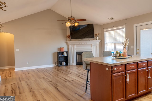 kitchen featuring arched walkways, lofted ceiling, light wood-style flooring, a kitchen breakfast bar, and a fireplace