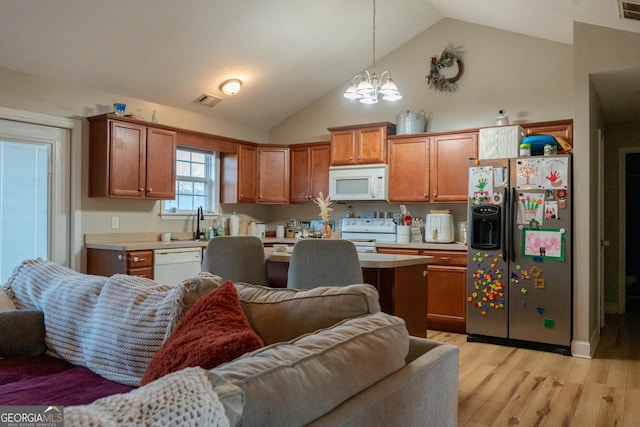 kitchen featuring lofted ceiling, hanging light fixtures, light wood-type flooring, a notable chandelier, and white appliances