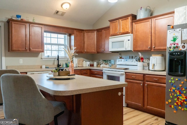 kitchen featuring a kitchen bar, sink, light hardwood / wood-style flooring, a kitchen island, and white appliances