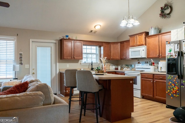 kitchen featuring a breakfast bar, a center island with sink, light wood-type flooring, pendant lighting, and white appliances