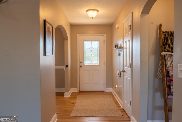 doorway with arched walkways, baseboards, a textured ceiling, and light wood finished floors