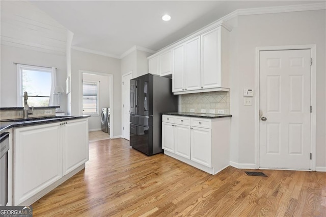 kitchen featuring white cabinets, backsplash, washing machine and clothes dryer, black fridge, and light hardwood / wood-style flooring