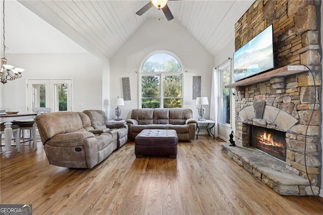 living room with ceiling fan with notable chandelier, a fireplace, high vaulted ceiling, and light hardwood / wood-style flooring