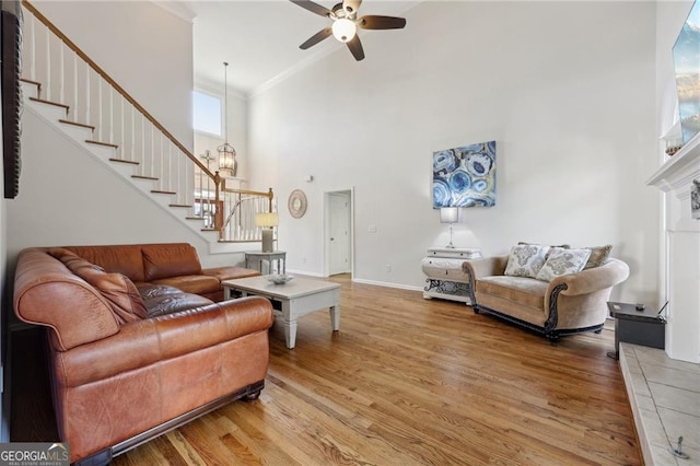 living room with ornamental molding, a tile fireplace, hardwood / wood-style flooring, ceiling fan with notable chandelier, and a high ceiling