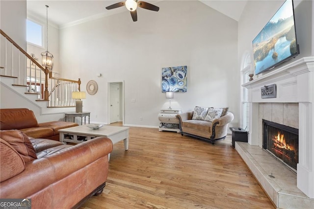 living room featuring crown molding, light hardwood / wood-style flooring, a high ceiling, a fireplace, and ceiling fan with notable chandelier