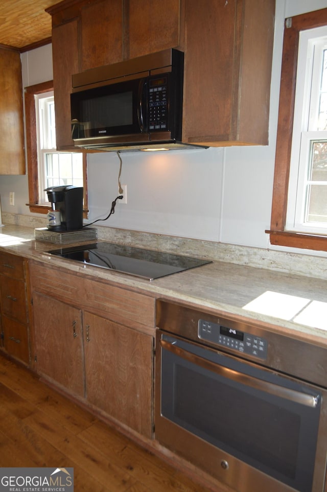 kitchen with wall oven, black electric stovetop, and hardwood / wood-style flooring