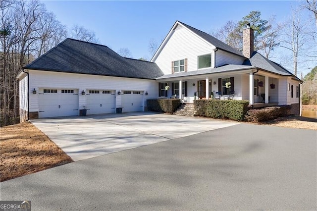 view of front of property featuring covered porch, driveway, a chimney, and a garage