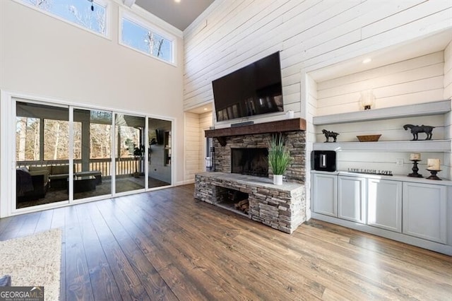 unfurnished living room featuring a healthy amount of sunlight, a towering ceiling, a fireplace, and wood finished floors