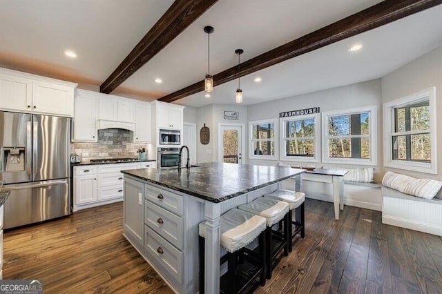 kitchen with stainless steel appliances, white cabinets, dark stone countertops, dark wood finished floors, and a center island with sink