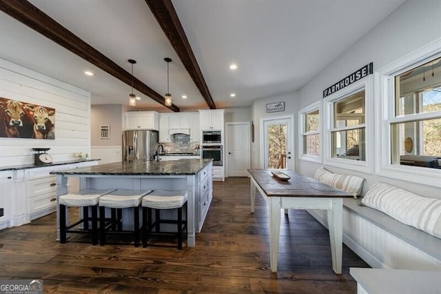 3055 Spring Hill Dr, Monroe, GA 30656 - kitchen with stainless steel appliances, beamed ceiling, white cabinetry, a breakfast bar area, and dark stone counters