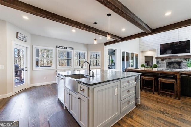 kitchen with dark wood-style flooring, open floor plan, beamed ceiling, an island with sink, and pendant lighting