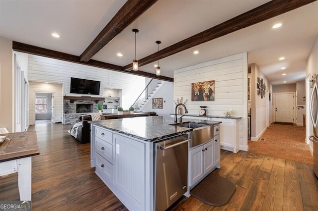 kitchen featuring a kitchen island with sink, a fireplace, white cabinetry, dishwasher, and dark stone countertops