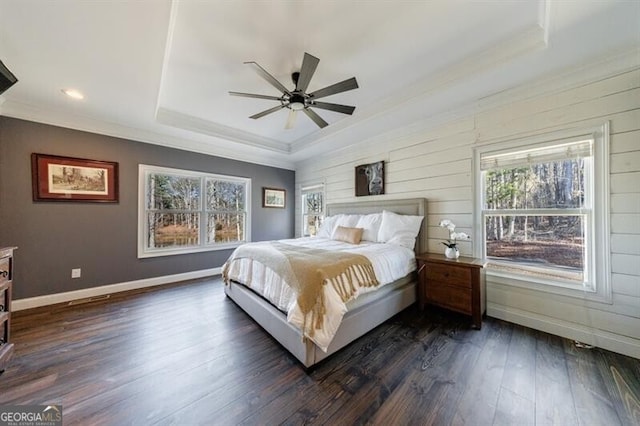 bedroom with dark wood-type flooring, a raised ceiling, and multiple windows