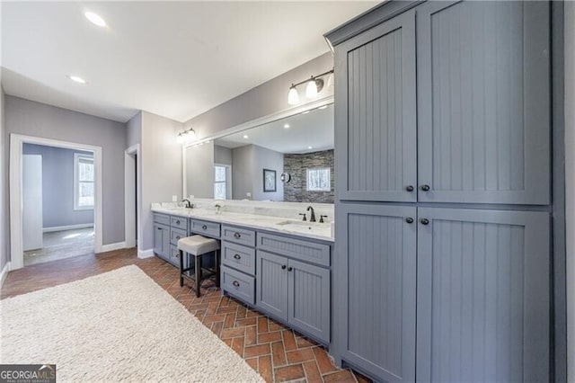 full bathroom featuring double vanity, a closet, baseboards, brick floor, and a sink