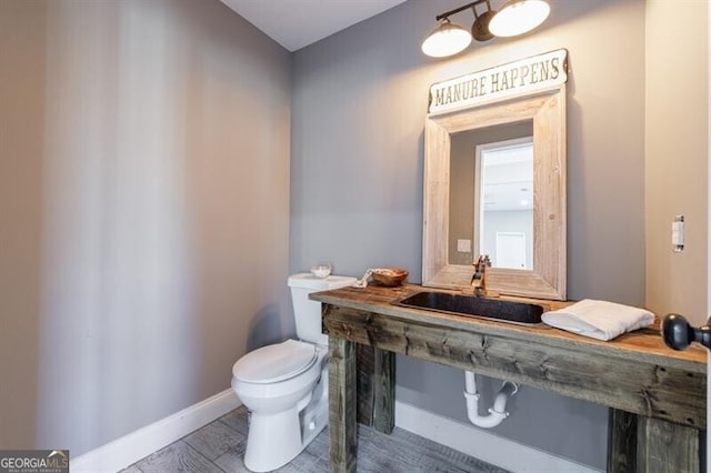 half bath with toilet, baseboards, and a sink