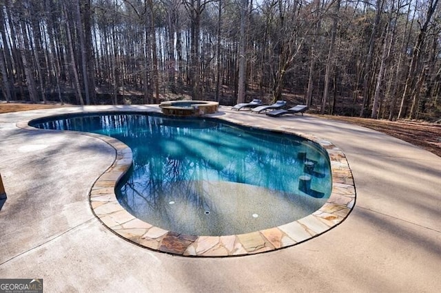 view of swimming pool with a pool with connected hot tub, a patio area, and a wooded view