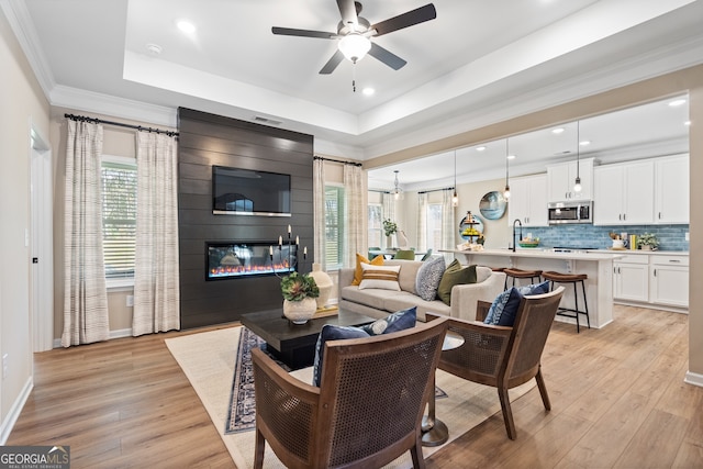 living room with ornamental molding, a tray ceiling, a fireplace, and light hardwood / wood-style floors