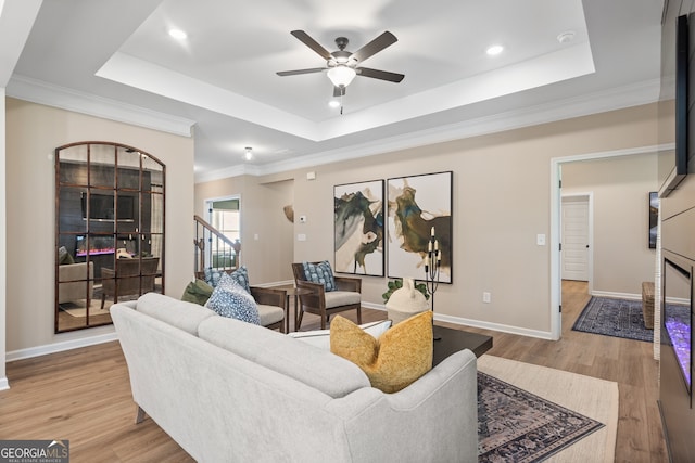 living room featuring ceiling fan, ornamental molding, a raised ceiling, and light wood-type flooring