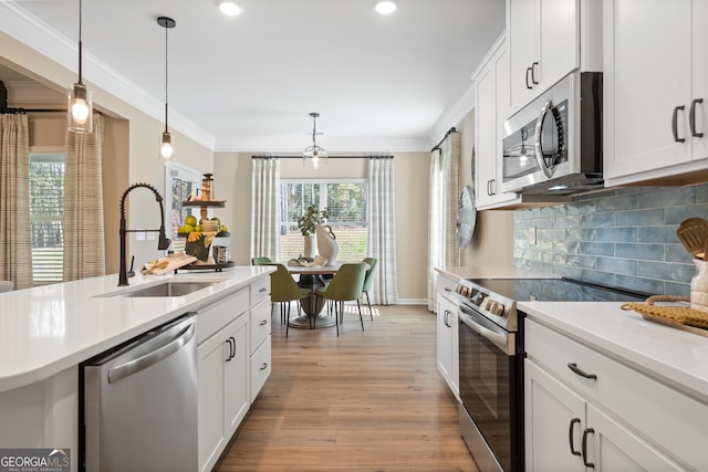 kitchen featuring sink, appliances with stainless steel finishes, white cabinetry, hanging light fixtures, and ornamental molding