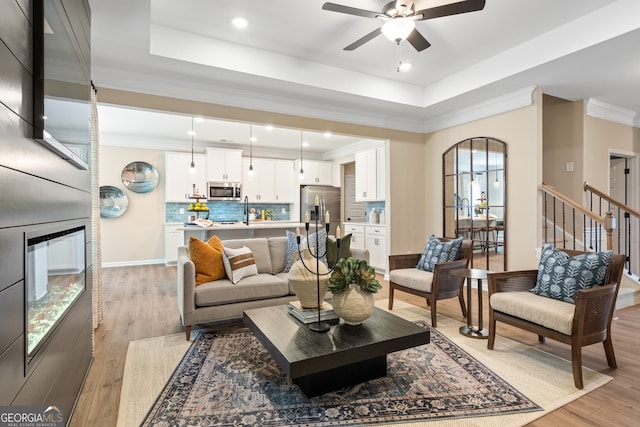 living room with sink, a tray ceiling, and light hardwood / wood-style floors