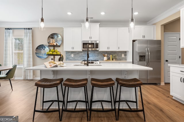 kitchen featuring a kitchen island with sink, hanging light fixtures, white cabinetry, and appliances with stainless steel finishes