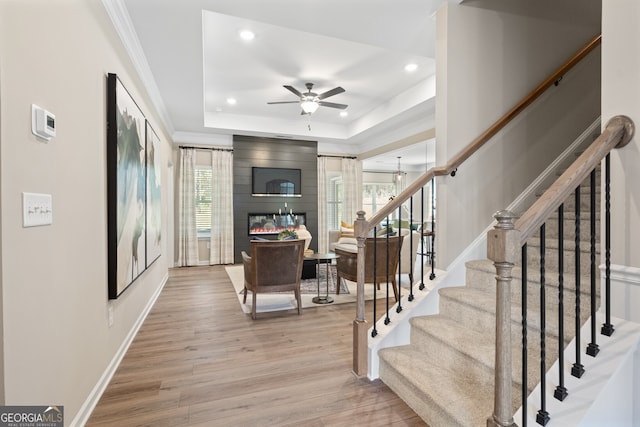 interior space with crown molding, ceiling fan, hardwood / wood-style floors, a fireplace, and a raised ceiling