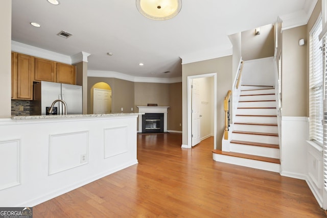 kitchen with backsplash, stainless steel fridge, crown molding, light stone countertops, and light wood-type flooring